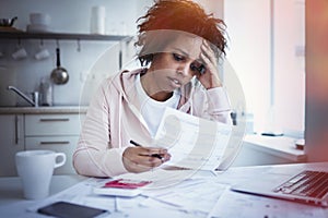 Upset african american woman at kitchen table with laptop, dealing with financial stress