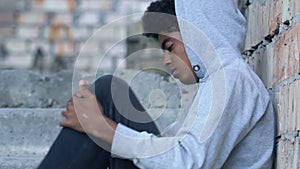 Upset Afro-American teen refugee holding knees, sitting in abandoned building