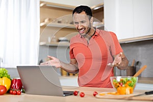 Upset angry young black man in red t-shirt gesturing with hands at computer, has problems with service