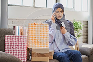 Upset Arabian woman holding a credit card and talking on the phone