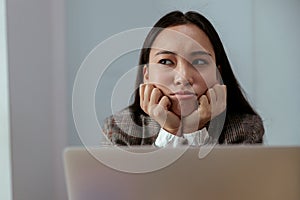 Upset asian business woman working on laptop in office and looks away