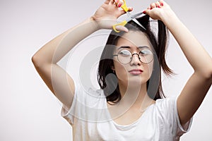 Upset Asian girl having trouble with long hair, cutting split ends with scissors