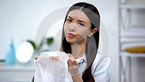 Upset asian housewife showing coffee stain on shirt at camera, laundry service