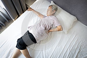 Upset asian senior woman holding hips or waist with her hand while rest in bed,painful facial expression from inflamed muscles,