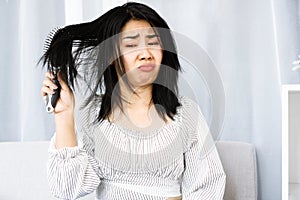 Upset Asian woman using comp brushing her dry ,damaged hair unhappy with messy hair photo