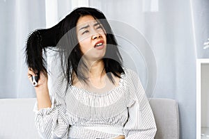 Upset Asian woman using comp brushing her dry ,damaged hair unhappy with messy hair photo