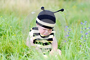 Upset baby in bee costume on the meadow