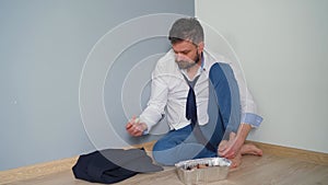 Upset bearded man in untidy formal clothes is sitting in an empty apartment. He has nothing to eat. He finds money in