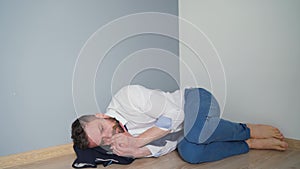 Upset bearded man in untidy formal clothes is sitting lies on the floor in an empty apartment. The effects of the Covid