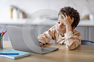 Upset black schoolboy tired of doing homework on laptop