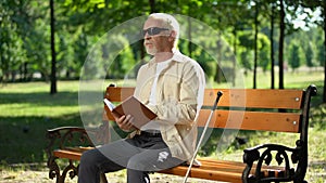 Upset blind retired man bored with braille book, feeling depressed alone in park