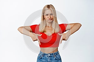 Upset blond woman grimacing, pointing fingers down at something bad, feel troubled by showing disappointing announcement