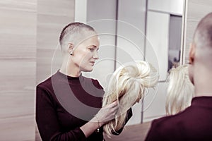 Upset bold woman holding her artificial hair