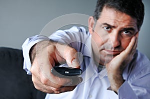 Upset and bored man holding tv remote control zapping TV Channel