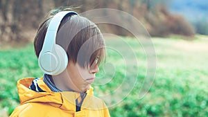 Upset boy with headphones on the walk. Lifestyle, childhood and emotions. Sad boy listening to music at nature