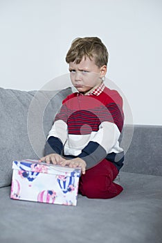 Upset boy sits with a gift on the bed