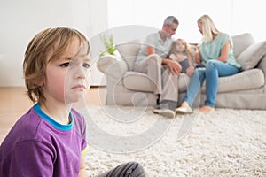 Upset boy sitting on floor while parents enjoying with sister