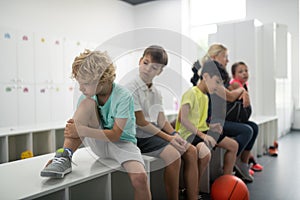 Upset boy sitting near his classmates on a bench.