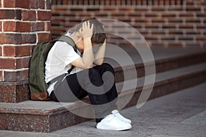 Upset boy sitting at school and crying after bullying by pupils classmates