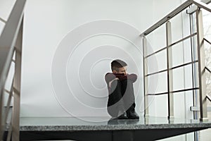 Upset boy sitting on staircase indoors