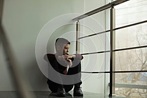 Upset boy sitting on staircase indoors. Space