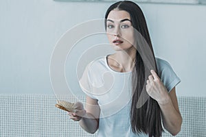 upset brunette woman holding hairbrush and looking at camera hair