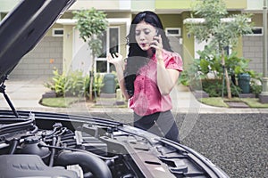 Upset business woman talking on the phone asking for a mechanic help to fix broken down car