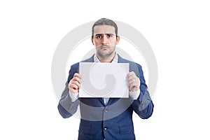 Upset businessman holding a blank paper sheet with copy space, looking sad and disappointed to camera, isolated on white