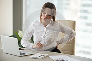 Upset businesswoman feeling back pain touching aching muscles in