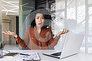 Upset businesswoman sitting at the table in the office, throwing her hands indignantly, confused by what happened