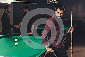 upset caucasian man with cue beside pool table at bar