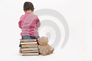 Upset child sitting on books with her teddybear