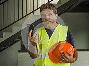Upset construction worker or stressed contractor man in hardhat and vest talking on mobile phone unhappy in stress messing with