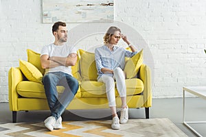 Upset couple sitting after argue on couch in front of wall