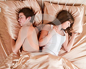 Upset couple sleeping separately on their bed