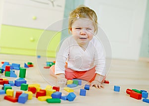 Upset crying baby girl with educational toys. Sad tired or hungry alone healthy child sitting near colorful different