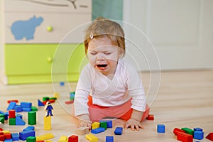 Upset crying baby girl with educational toys. Sad tired or hungry alone healthy child sitting near colorful different