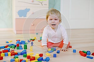 Upset crying baby girl with educational toys. Sad tired or hungry alone healthy child sitting near colorful different