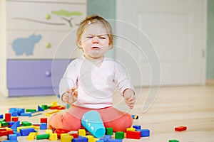 Upset crying baby girl with educational toys. Sad tired or hungry alone healthy child sitting near colorful different