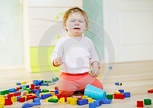 Upset crying baby girl with educational toys. Sad tired or hungry alone healthy child sitting near colorful different