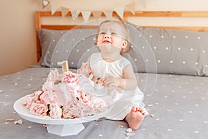 upset crying Caucasian blonde baby girl in white dress celebrating her first birthday