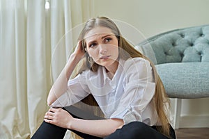 Upset crying young woman sitting at home on the floor.