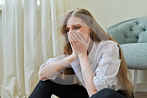 Upset crying young woman sitting at home on the floor.