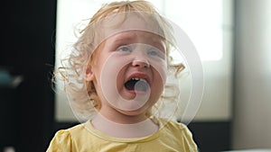 Upset curly haired child crying, portrait. capricious blonde girl in yellow T-shirt is furious and demands attention to