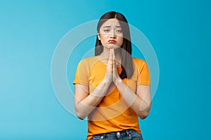 Upset cute silly asian girl praying, plead for help, pouting frowning need, make pitty face, hold hands pray begging for photo