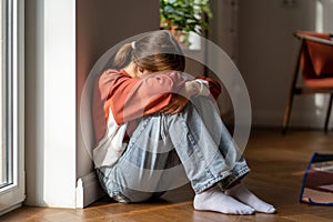 Upset depressed teenage girl sitting alone on floor and crying