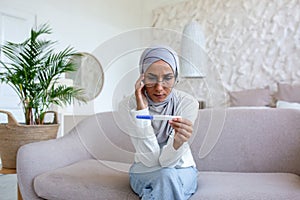 Upset and depressed woman sitting on sofa at home, muslim woman got bad pregnancy test result, woman in hijab