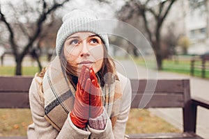 Upset devastated young woman sitting on bench in autumn park crying and praying. Mental health and religion