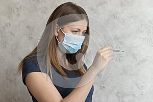 Upset, displeased girl in medical face mask with thermometer. Flu, cold, virus, fever and coronavirus symptoms. Woman measured her