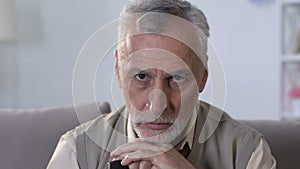 Upset elderly man with walking stick sitting on sofa in rehabilitation center